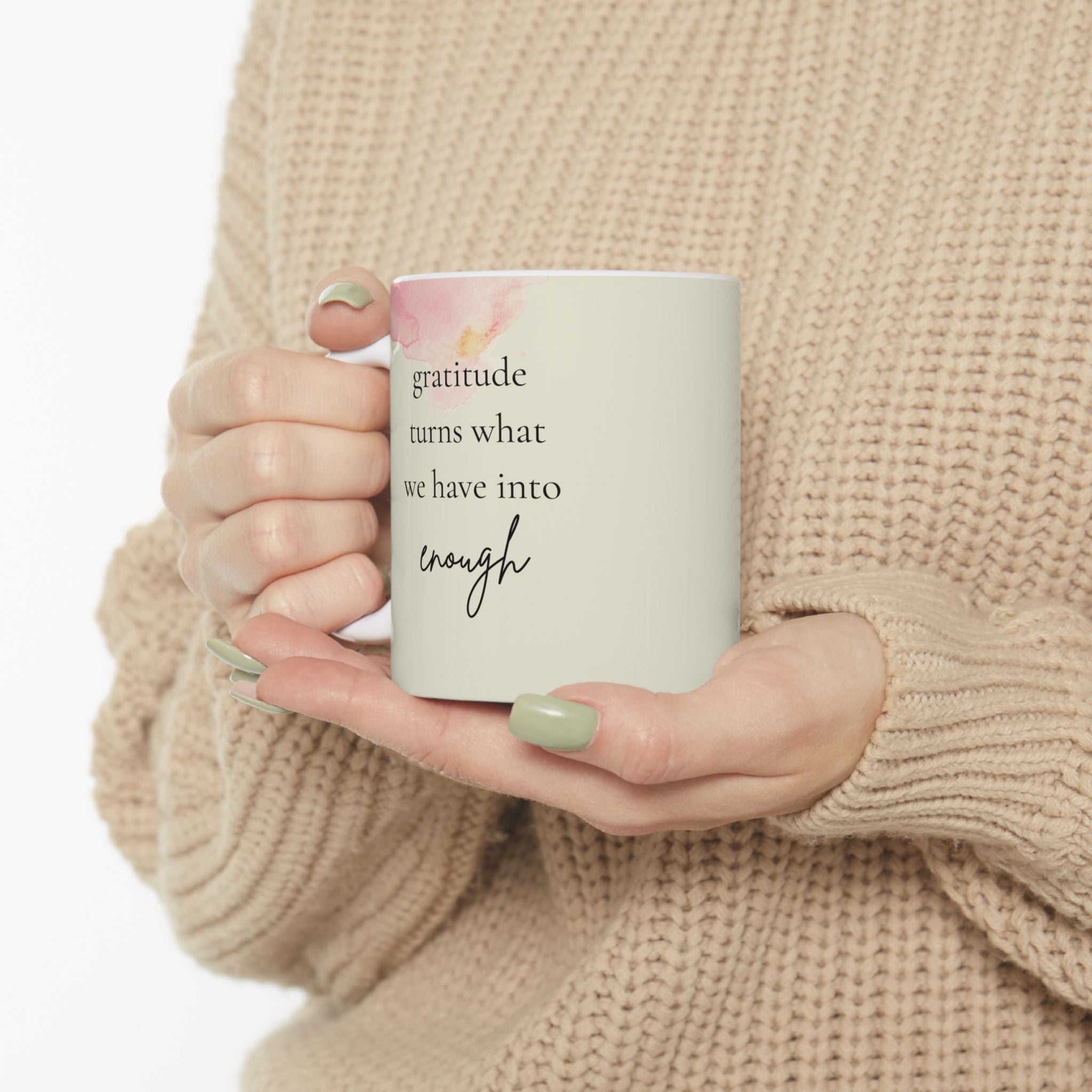 The image shows a person holding a white ceramic mug with a motivational quote. The quote on the mug reads, "Gratitude turns what we have into enough." The mug has a pink floral design near the rim.