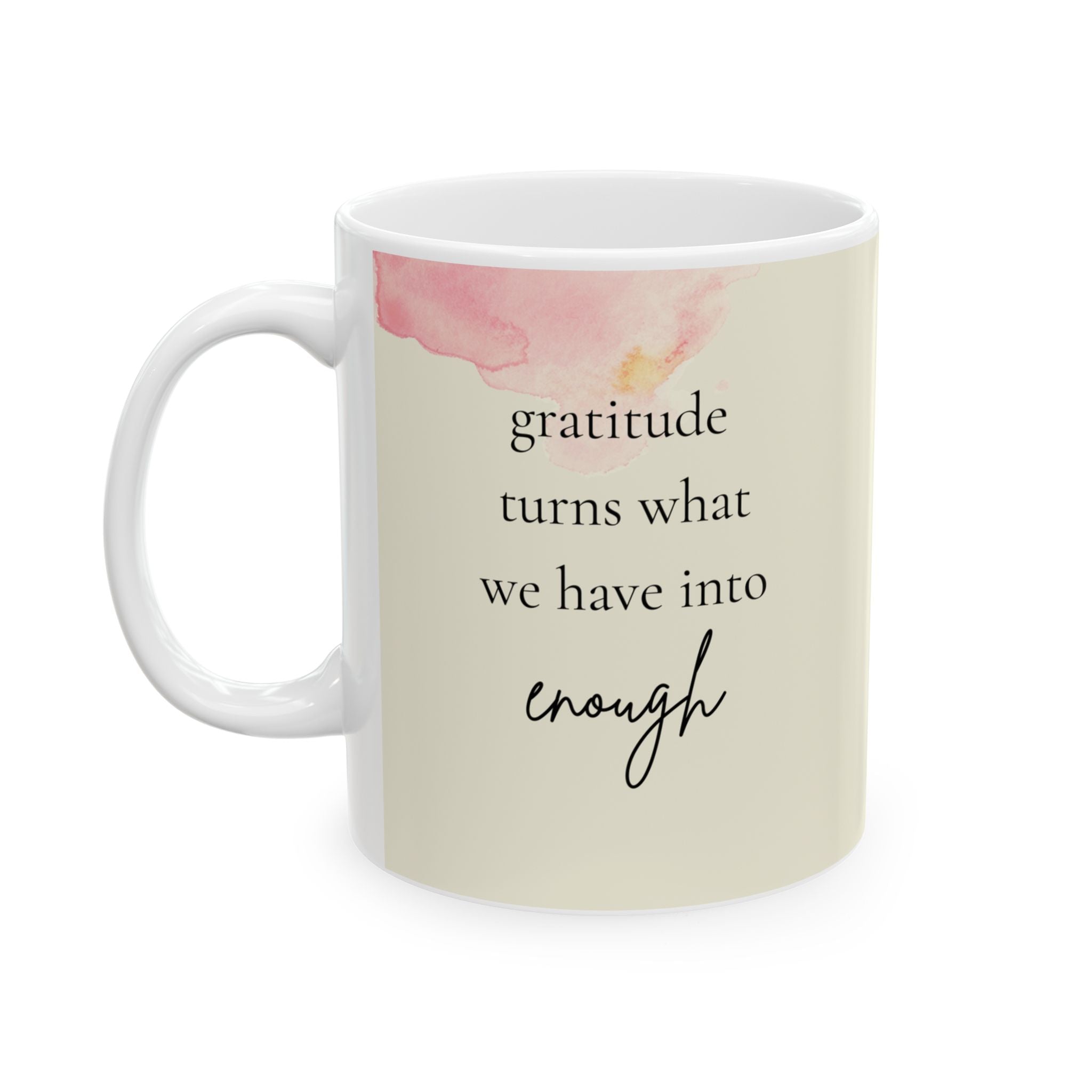 The image shows a white ceramic mug with a handle, featuring a motivational quote and a soft pink watercolor design. The quote reads "gratitude turns what we have into enough" in black lettering, with "enough" in a cursive font. A delicate pink watercolor splotch is visible near the rim on the left side of the mug.